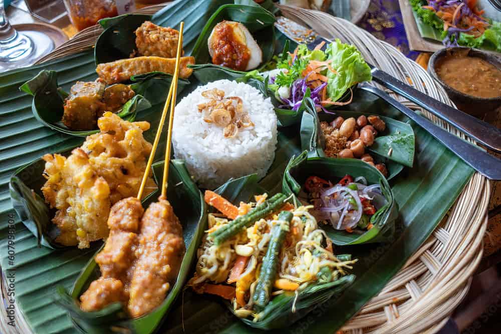 An Indonesian dinner consisting of small dishes including satay, rice, tempeh, and salads.
