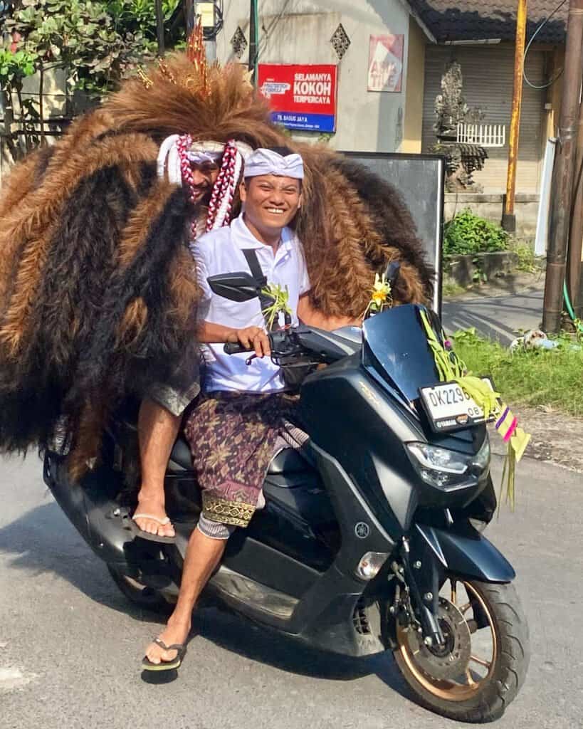 Traditional balinese dressed man with a Barong on a scooter.